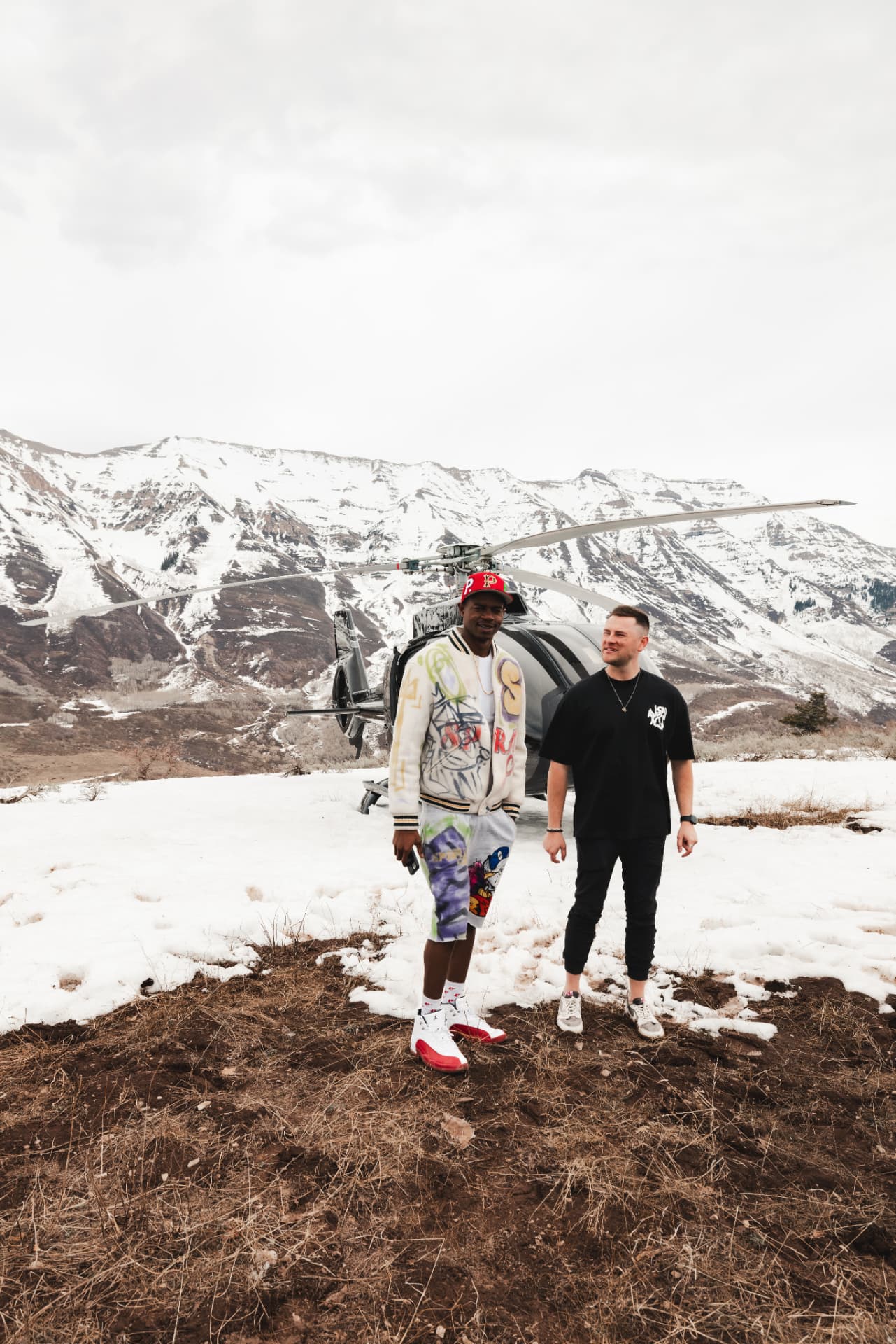 Athlete and Coinlete partner beside a helicopter in the mountains