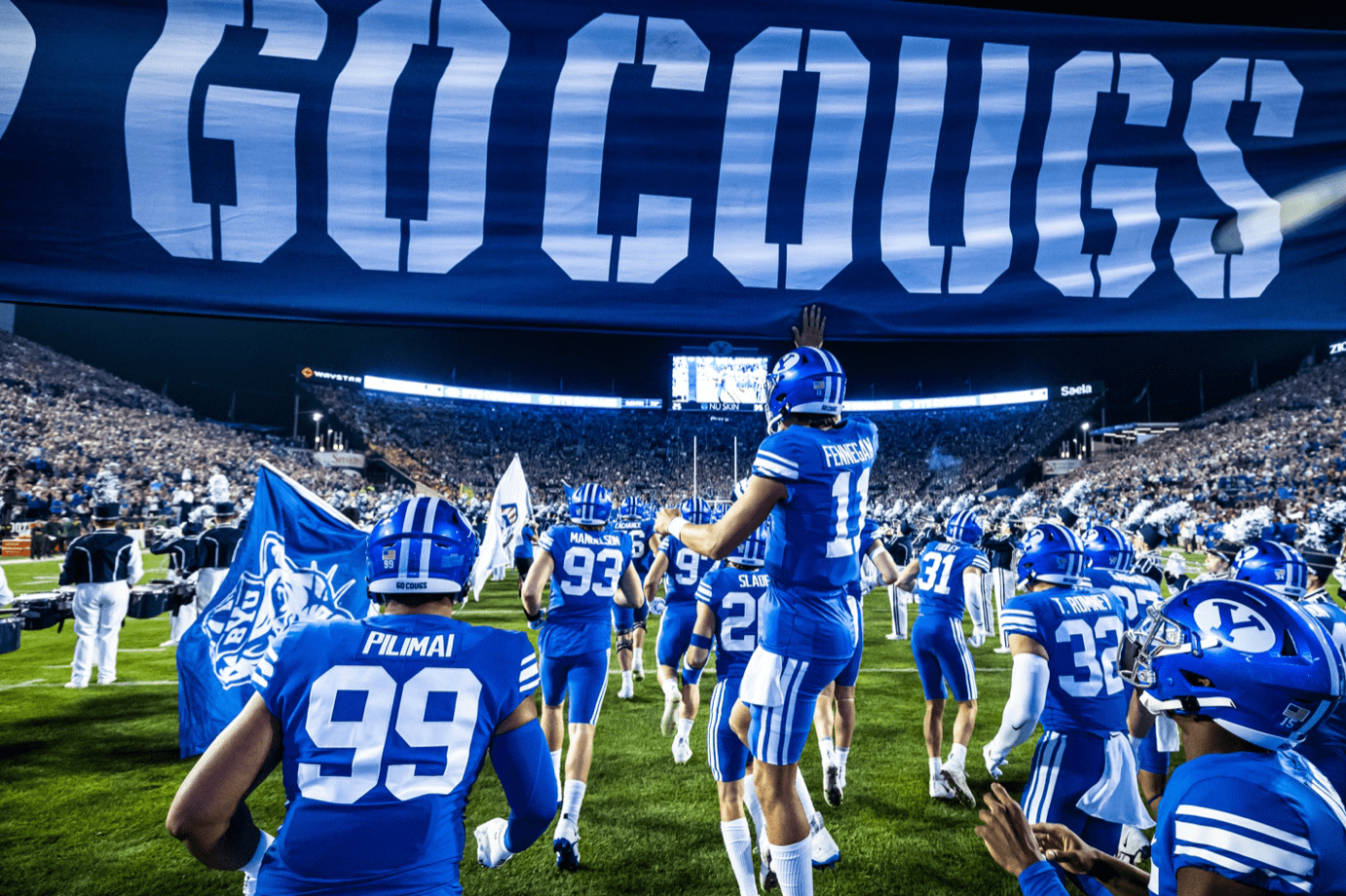 BYU football team running onto the field under the Go Cougs banner